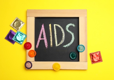 Photo of Colorful condoms and blackboard with word AIDS on yellow background, flat lay. Safe sex