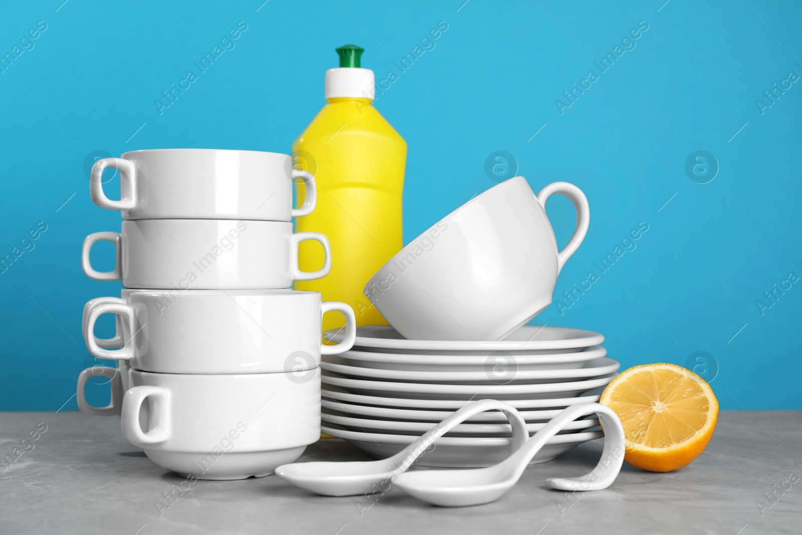 Photo of Clean tableware, dish detergent and lemon on grey table against light blue background