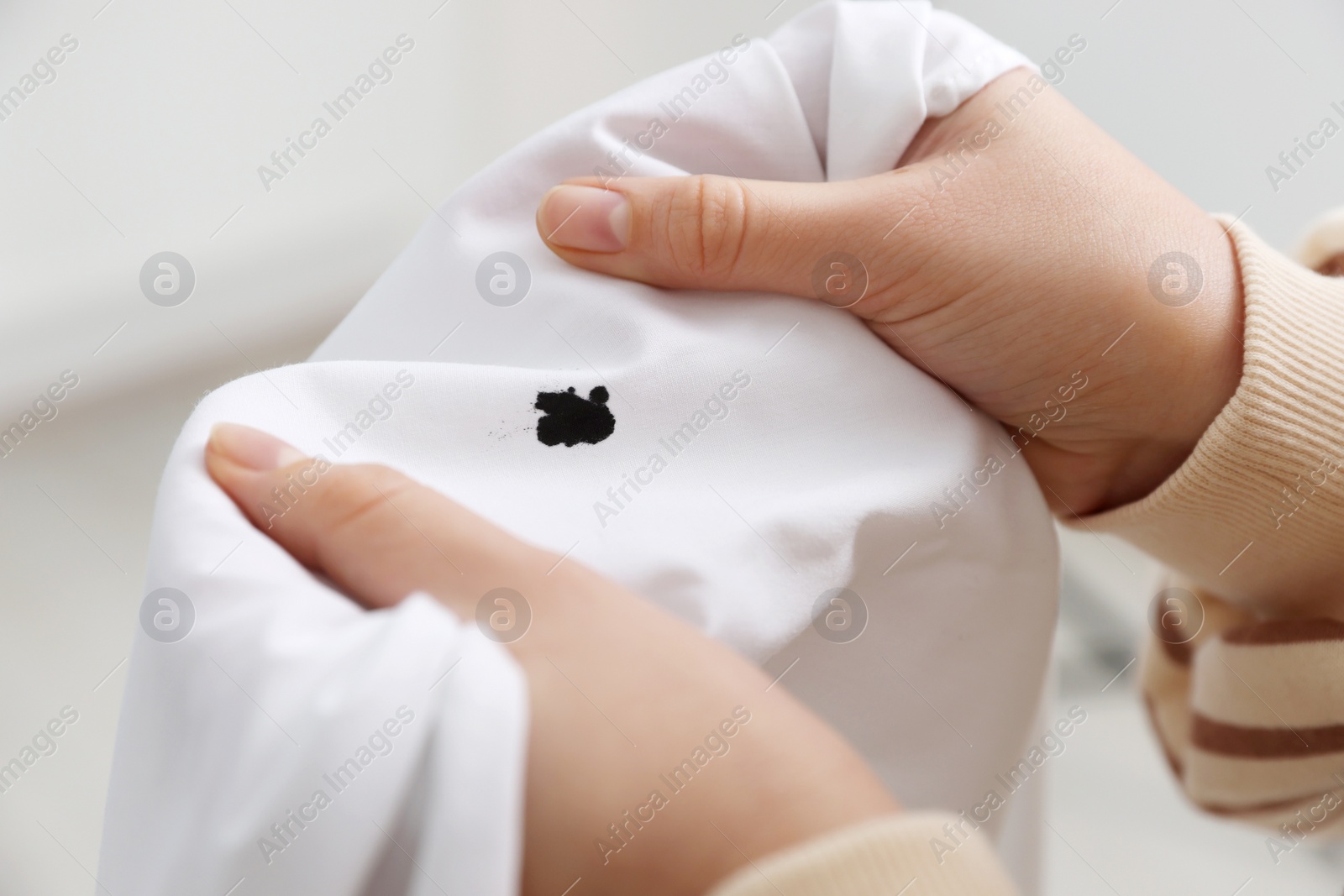 Photo of Woman holding white shirt with black ink stain on blurred background, closeup