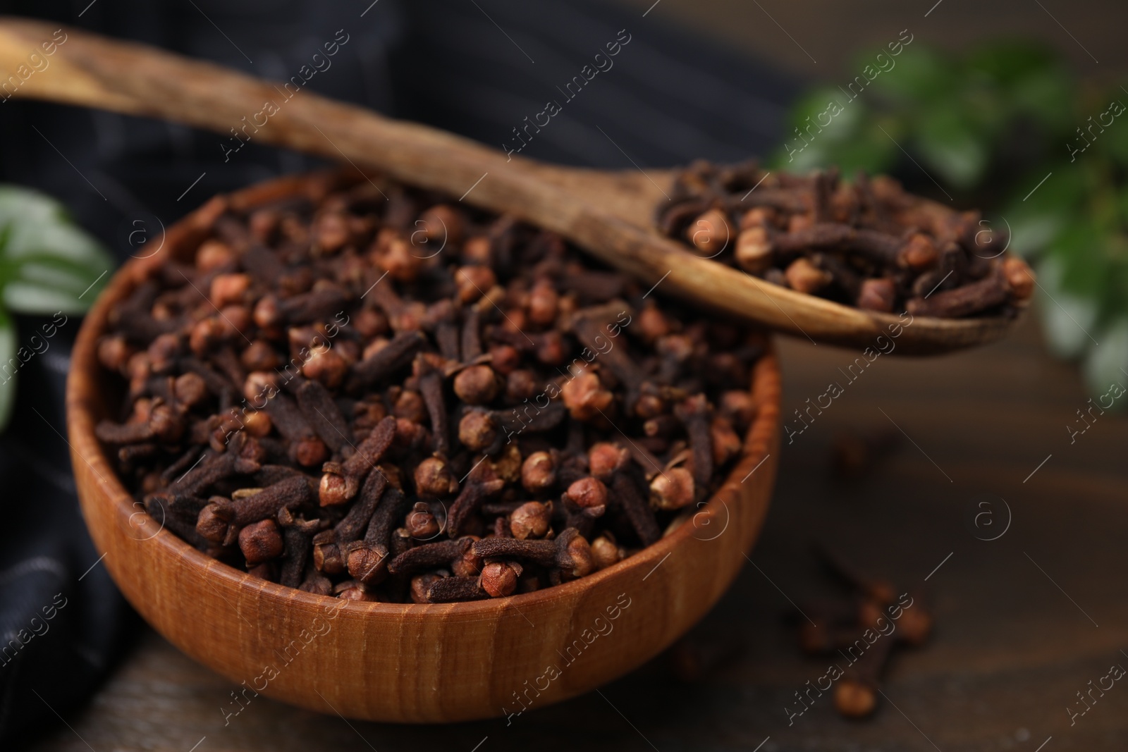 Photo of Bowl and spoon with aromatic cloves on wooden table, closeup