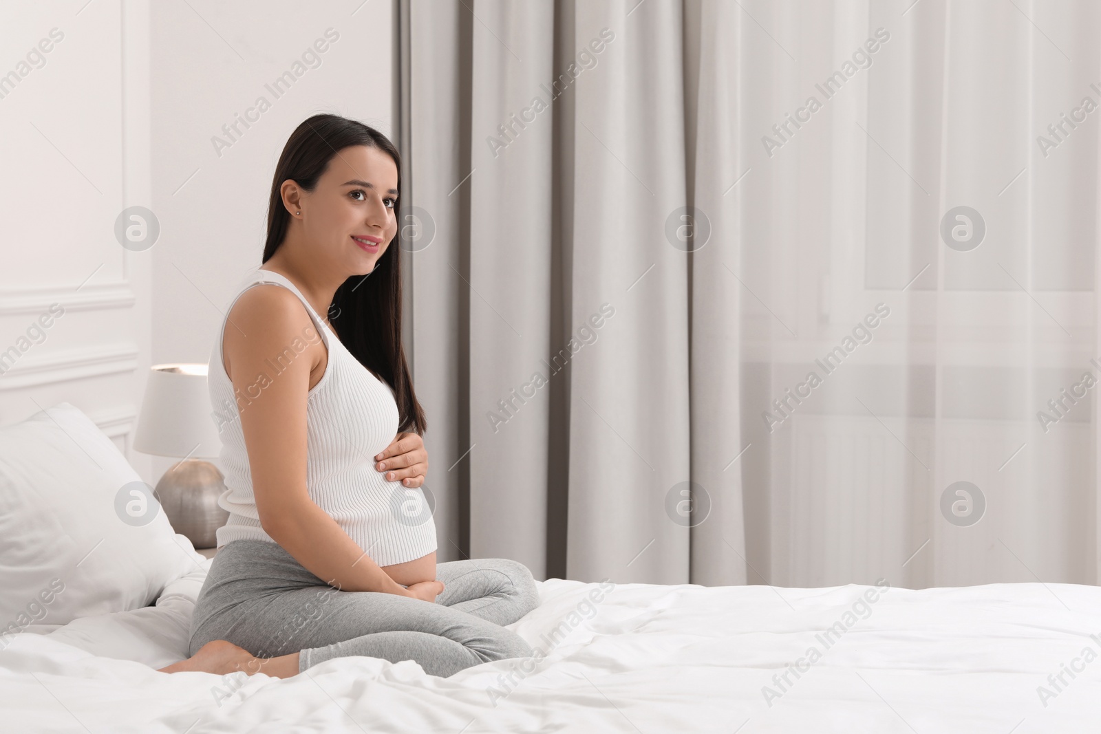 Photo of Beautiful pregnant woman on bed at home, space for text