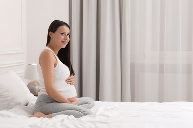 Photo of Beautiful pregnant woman on bed at home, space for text