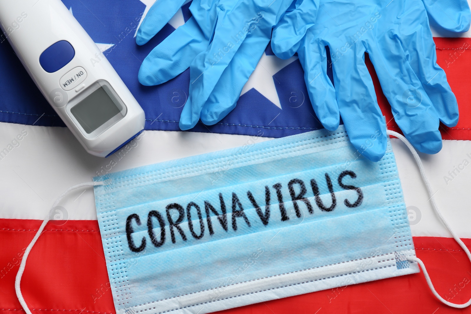 Photo of Word CORONAVIRUS written on protective mask, thermometer, gloves and American flag, flat lay. Covid-19 pandemic in USA