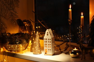 Photo of Many beautiful Christmas decorations, candlesticks and festive lights on window sill indoors