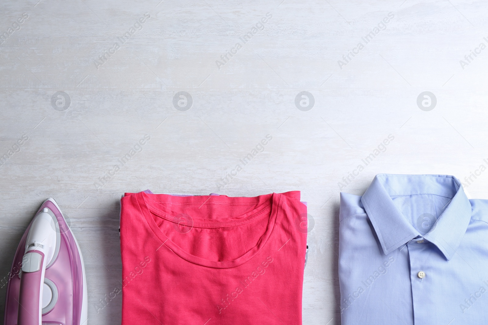 Photo of Flat lay composition with folded clothes and modern iron on light table. Space for text