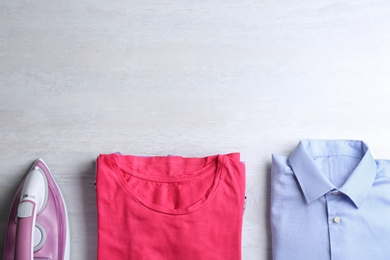 Photo of Flat lay composition with folded clothes and modern iron on light table. Space for text