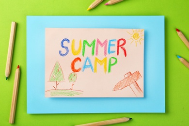 Photo of Paper with written text SUMMER CAMP, drawings and different pencils on color background, flat lay