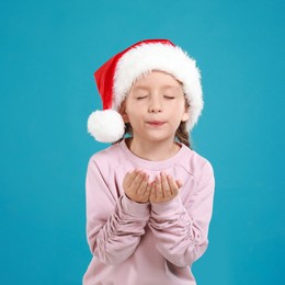 Image of Little child in Santa hat on light blue background. Christmas celebration