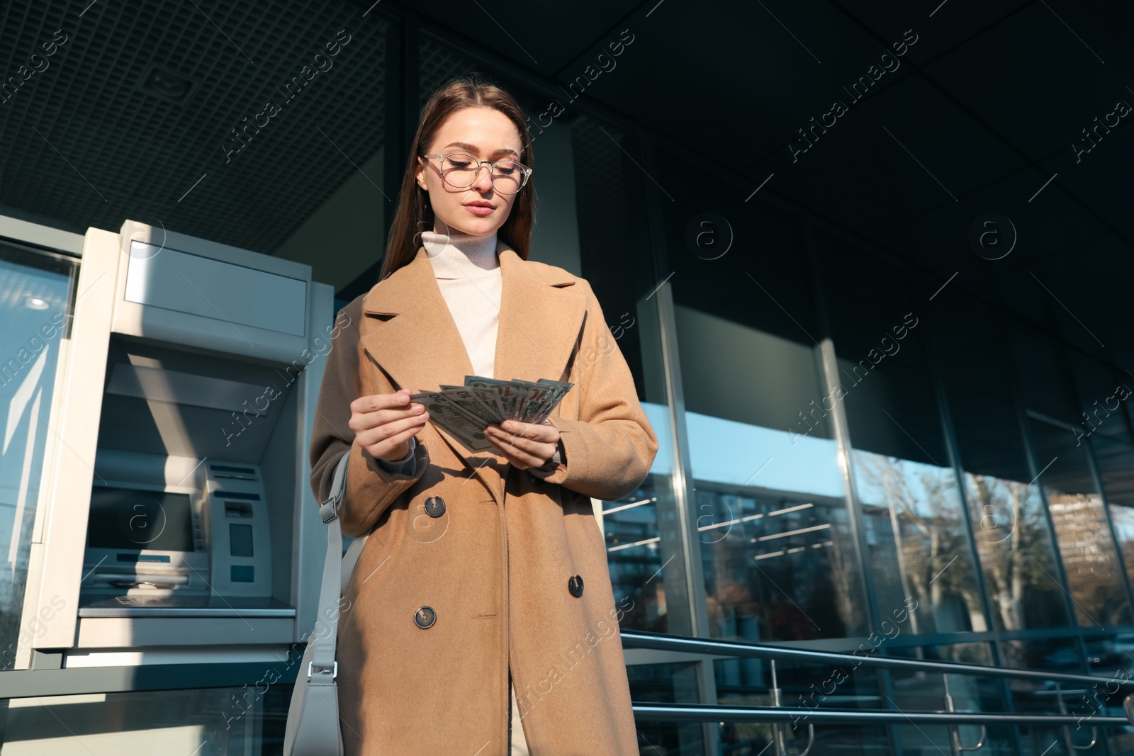 Photo of Young woman with money near cash machine outdoors