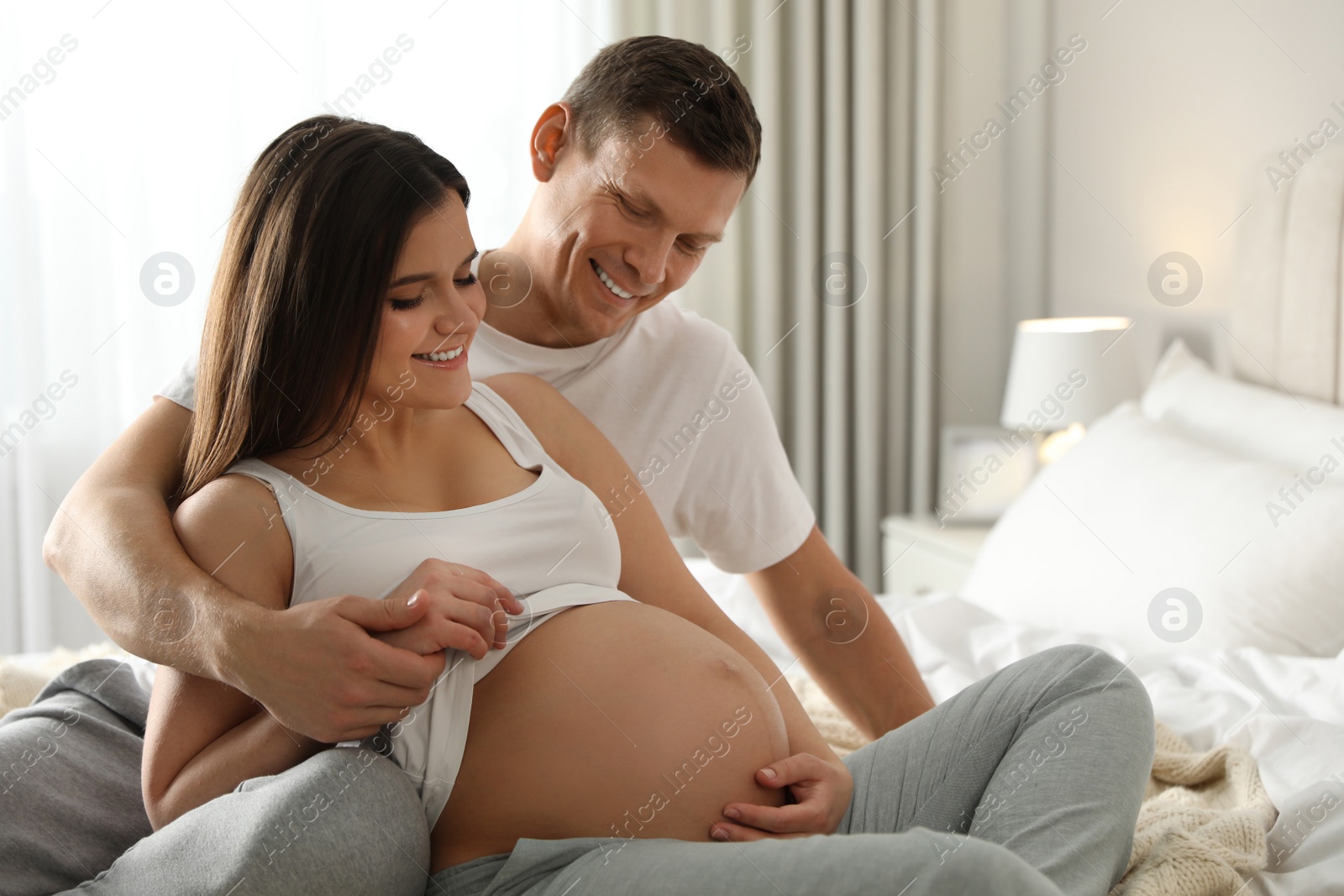 Photo of Young pregnant woman with her husband in bedroom