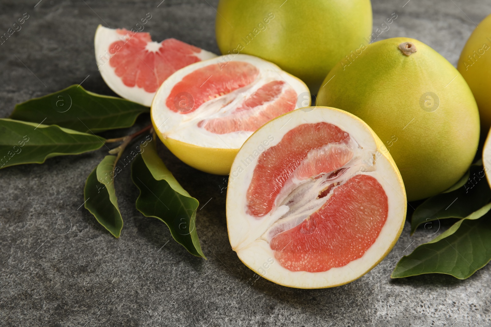 Photo of Fresh cut and whole pomelo fruits with leaves on grey table