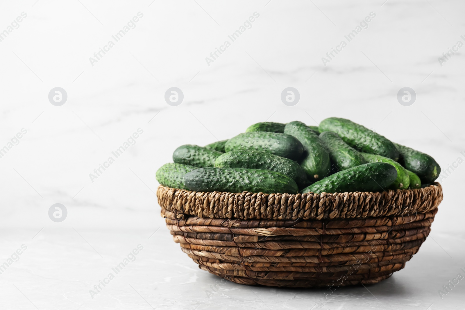 Photo of Fresh ripe cucumbers in wicker basket on marble table, space for text