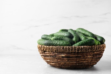 Photo of Fresh ripe cucumbers in wicker basket on marble table, space for text