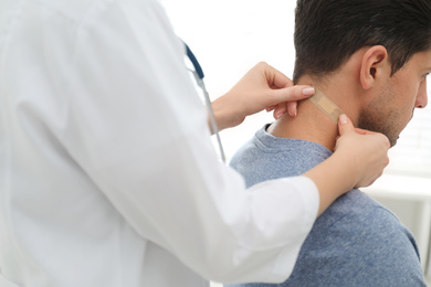 Photo of Doctor putting sticking plaster onto man's neck indoors, closeup