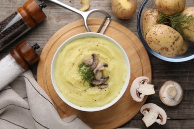 Bowl of tasty cream soup with mushrooms, dill and raw potatoes on wooden table, flat lay