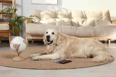 Photo of Cute golden retriever lying near passport, tickets and globe on floor in living room. Travelling with pet