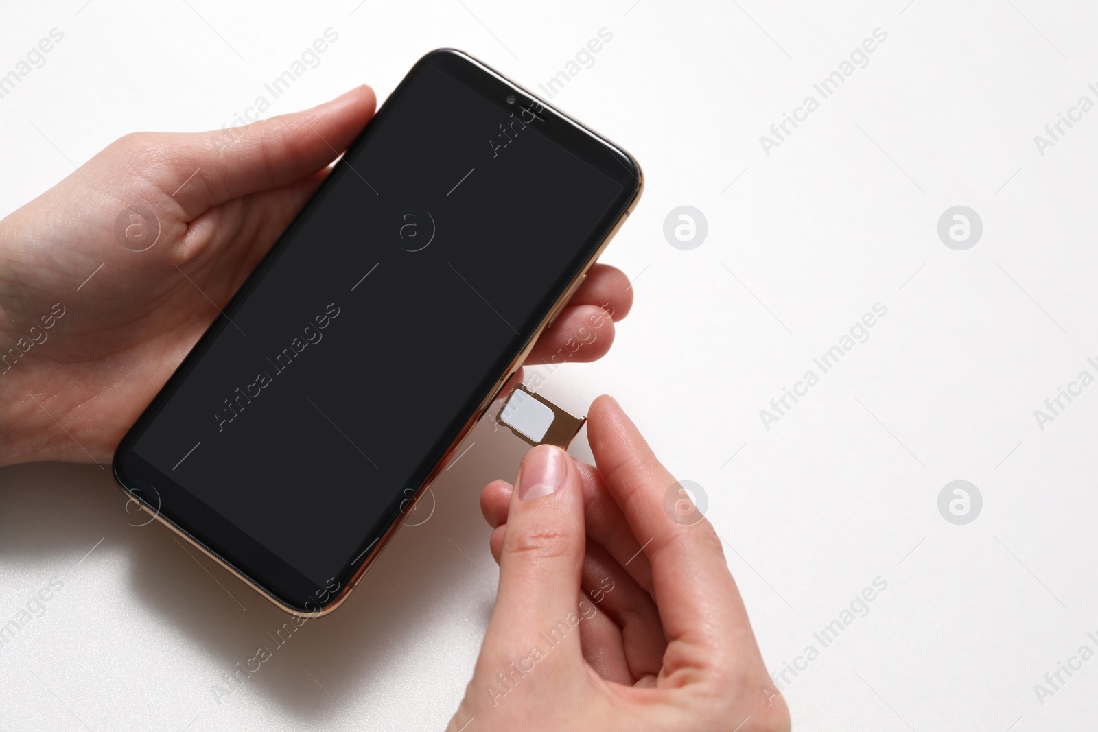 Photo of Woman putting SIM card tray in smartphone at white table, closeup