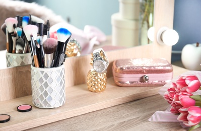 Holder with professional makeup brushes and tulip bouquet on wooden table