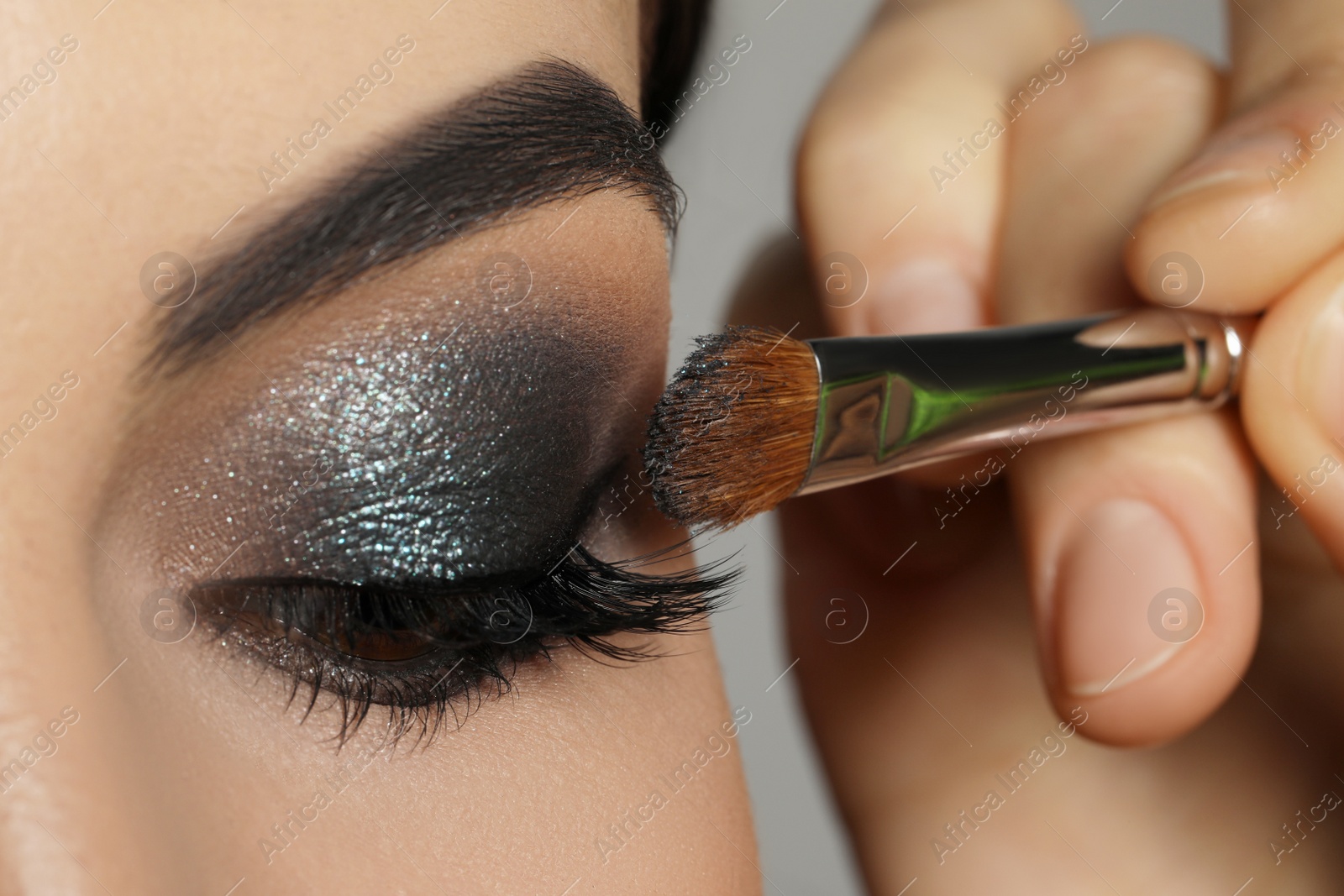 Photo of Applying dark eye shadow with brush onto woman's face, closeup. Beautiful evening makeup