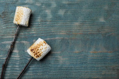 Photo of Sticks with roasted marshmallows on blue wooden table, flat lay. Space for text