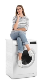 Young woman sitting on washing machine against white background. Laundry equipment