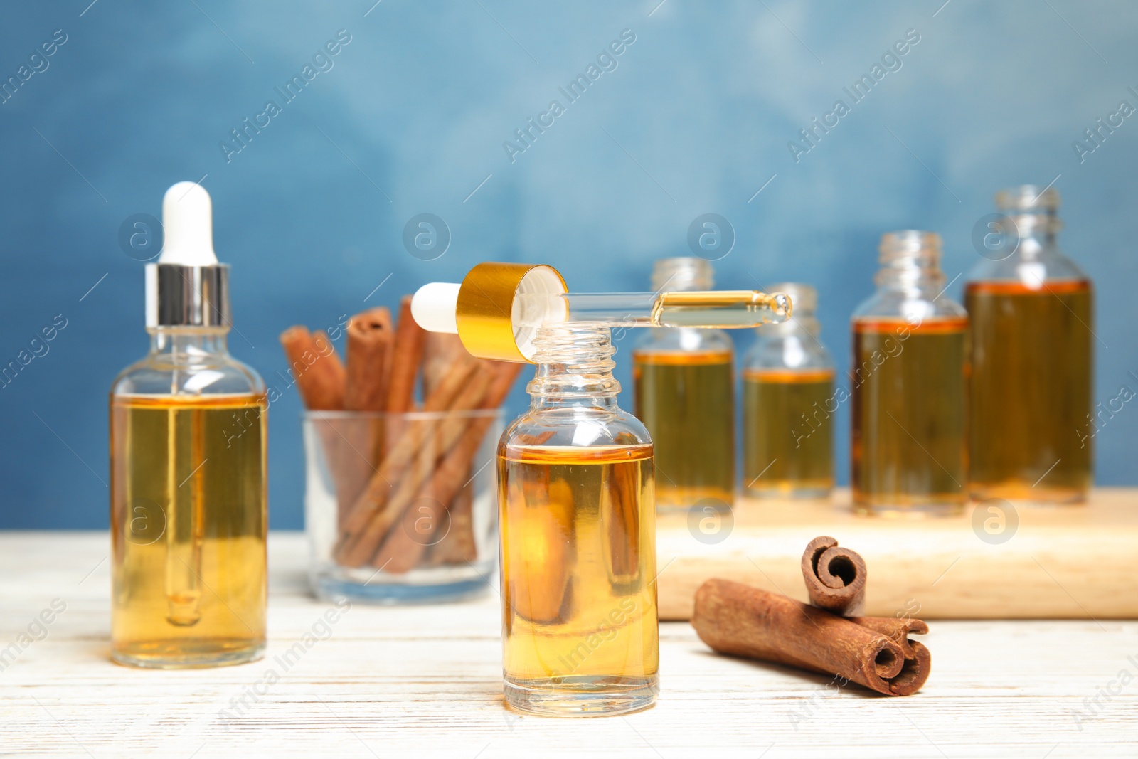 Photo of Bottles of essential oils and cinnamon sticks on table against blue background