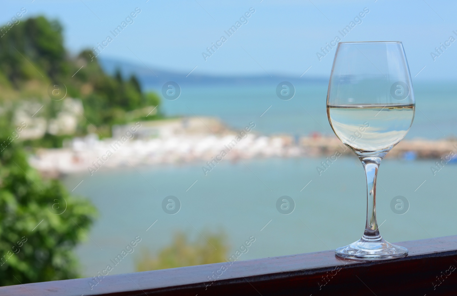 Photo of Glass with wine on railing near sea. Space for text