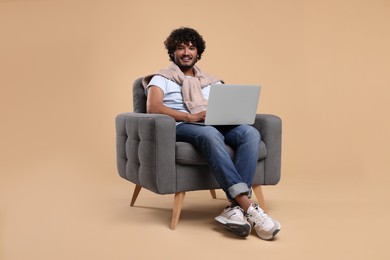 Smiling man with laptop sitting in armchair on beige background