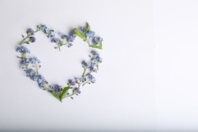 Heart made with beautiful forget-me-not flowers on white background, top view. Space for text