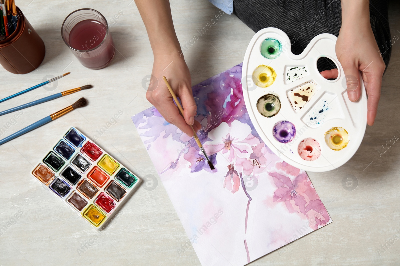 Photo of Woman painting flowers with watercolor on floor, top view