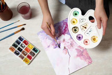 Woman painting flowers with watercolor on floor, top view