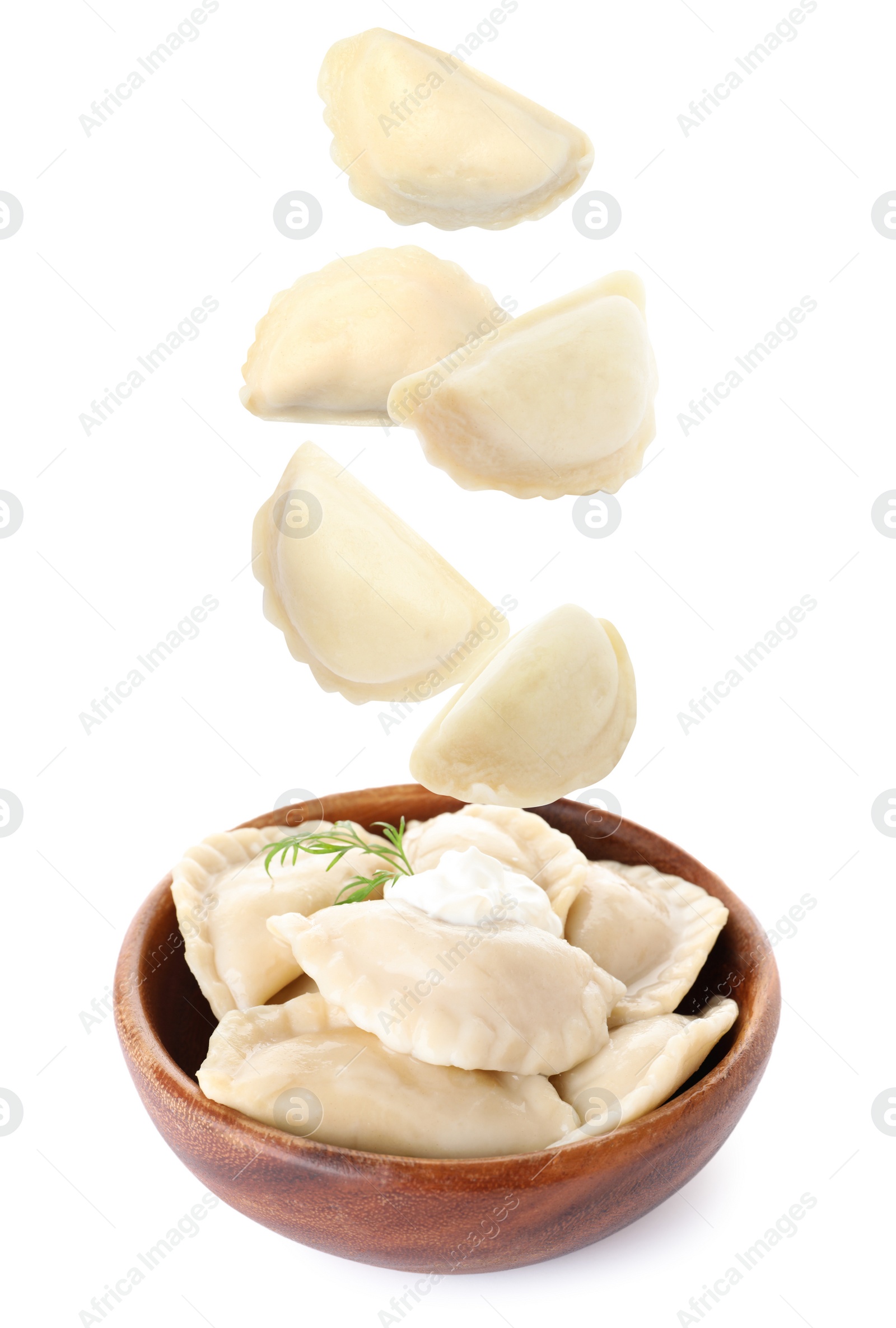 Image of Many tasty dumplings falling into wooden bowl on white background