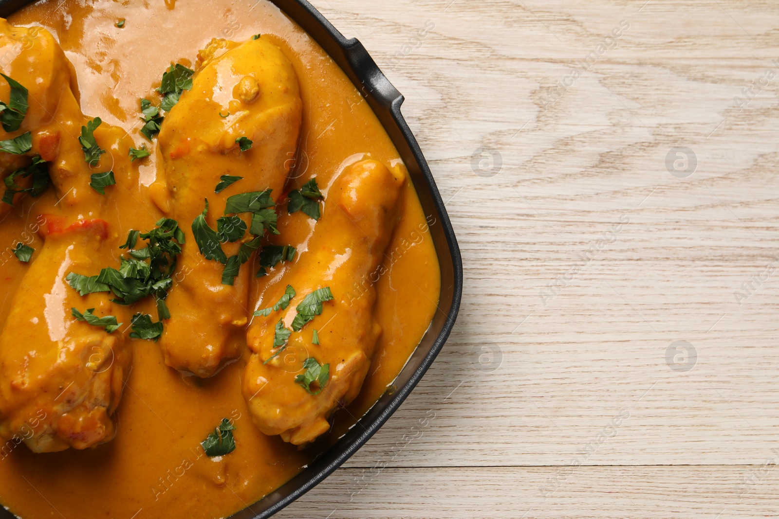 Photo of Tasty chicken curry with parsley on wooden table, top view. Space for text