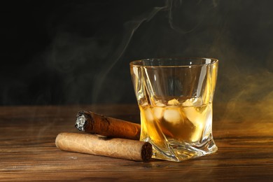 Photo of Glass of whiskey with ice cubes and cigars on wooden table