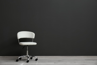 Photo of Comfortable office chair near black wall indoors. Space for text