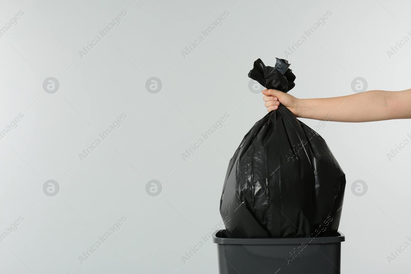 Photo of Woman holding trash bag full of garbage over bucket on light grey background, closeup. Space for text