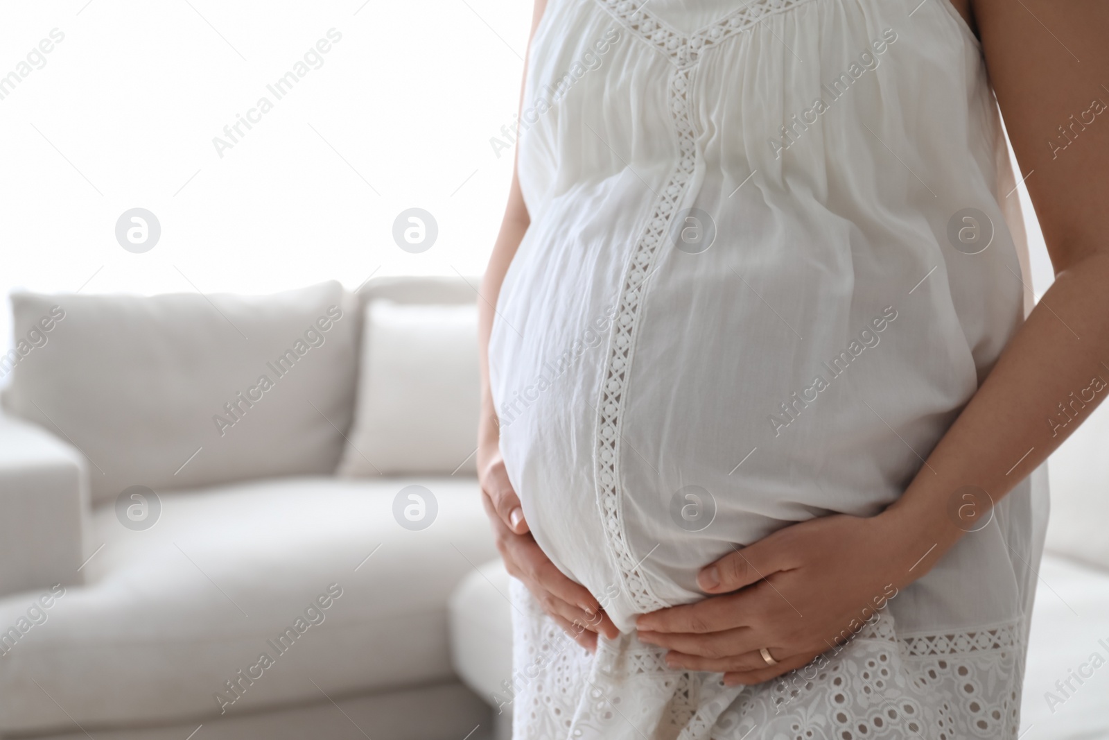 Photo of Pregnant young woman touching belly at home, closeup. Space for text