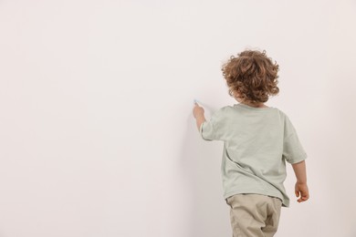 Photo of Little boy drawing on white wall indoors, back view. Space for text