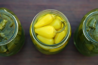 Photo of Glass jars of pickled green and yellow jalapeno peppers on wooden table, flat lay