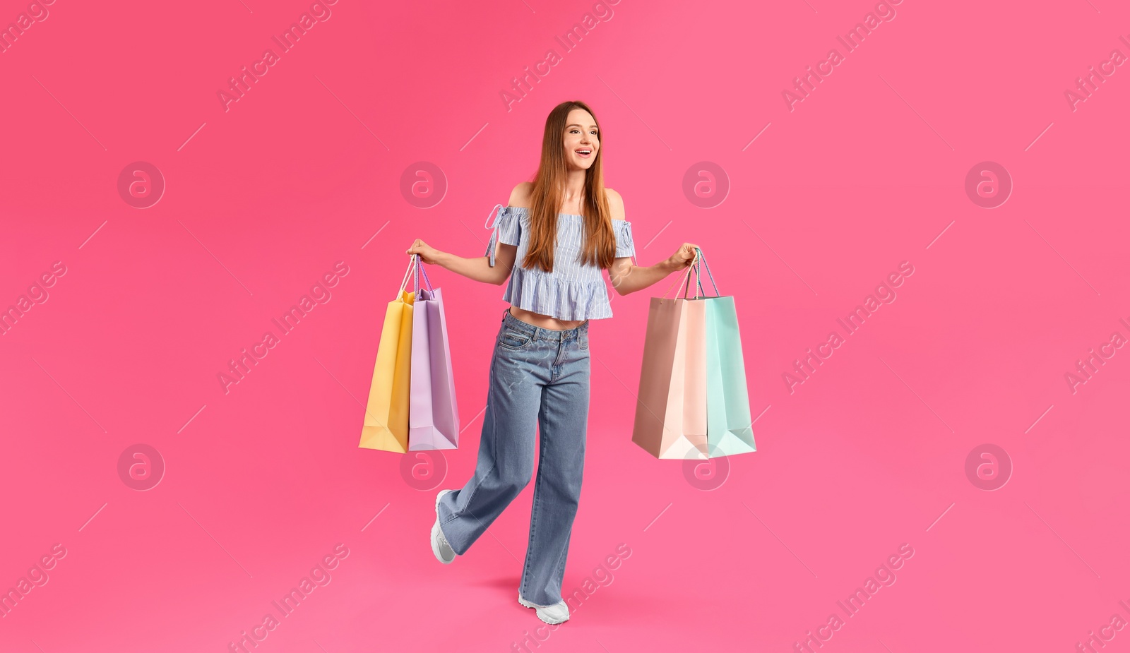 Photo of Beautiful young woman with paper shopping bags running on pink background