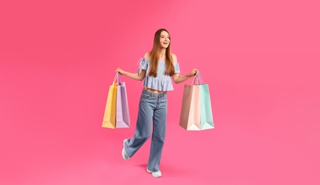 Photo of Beautiful young woman with paper shopping bags running on pink background