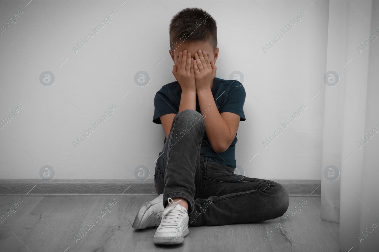 Photo of Sad little boy closing eyes with hands on floor indoors. Child in danger