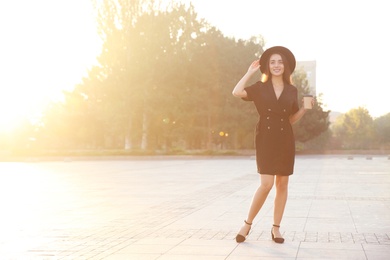 Photo of Beautiful young woman in stylish black dress and hat with cup of coffee on city street