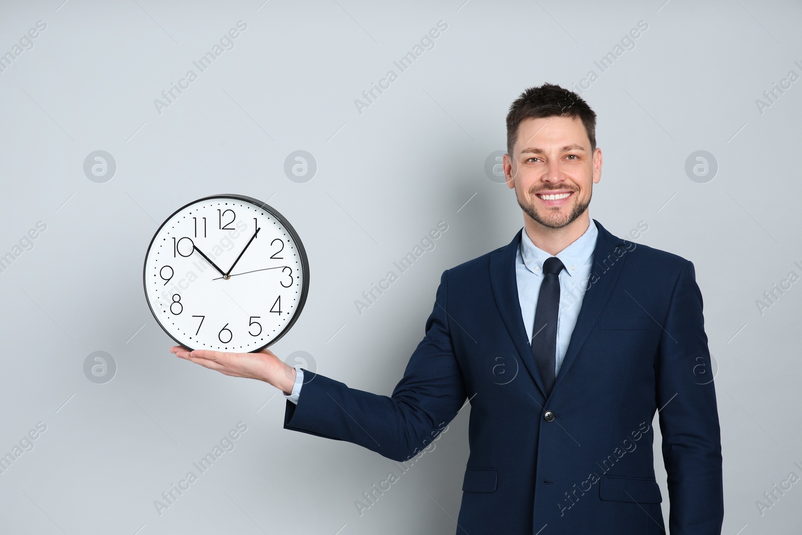 Photo of Happy businessman holding clock on grey background. Time management