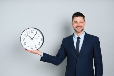Photo of Happy businessman holding clock on grey background. Time management