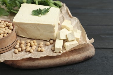 Photo of Pieces of delicious tofu with parsley and soy on black wooden table, closeup