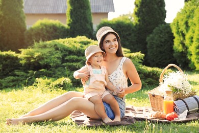 Mother with her baby daughter having picnic in garden on sunny day