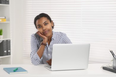 Photo of Sad African American intern working on laptop at white table in office. First work day
