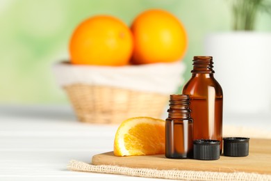 Bottles of essential oil and orange slice on white wooden table, space for text