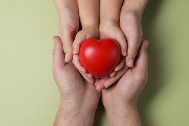 Parents and child holding red decorative heart on light green background, top view